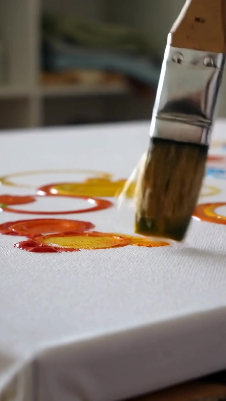 Video verticale: Pennello a setole piatte che intinge nel rosso e nel giallo su tela in studio, mescolando l'arancione