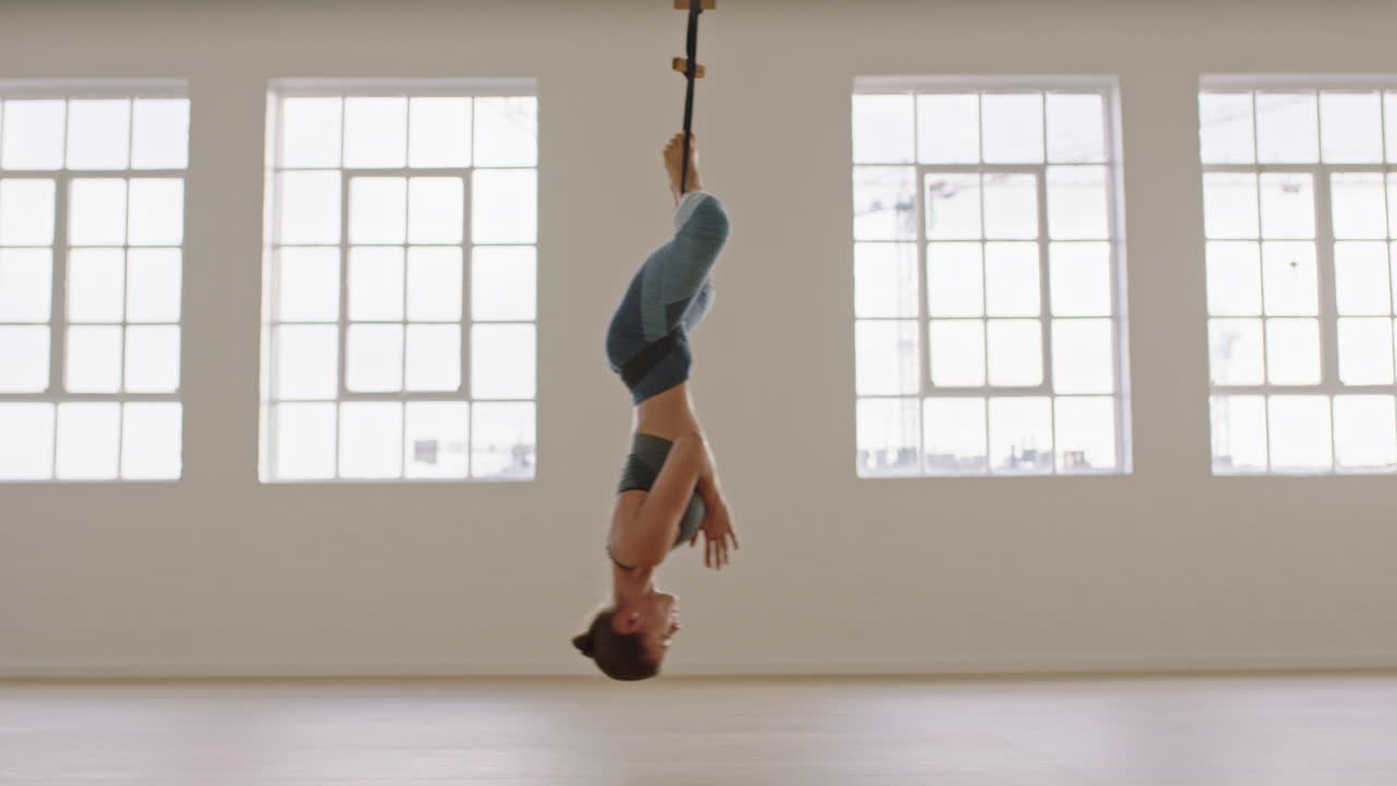 공중 요가 여성이 역전 나비 자세를 연습하고 하모크를 사용하여 거꾸로 매달려 건강한 피트니스 라이프 스타일을 즐기고 스튜디오에서 운동하고 해가 뜨면 명상하고 있습니다.