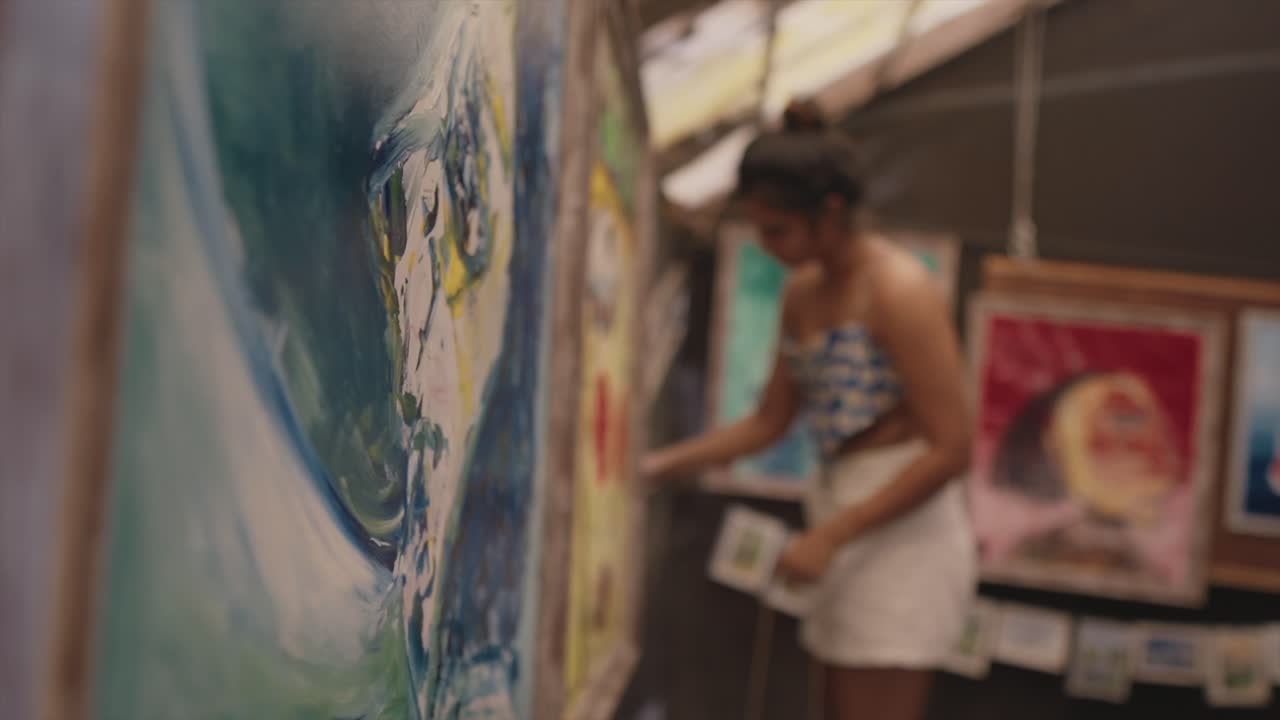 아름다운 미술품이 벽에 매달려 있고, 한 소녀가 배경에서 흐릿하게 작업하고 있습니다.