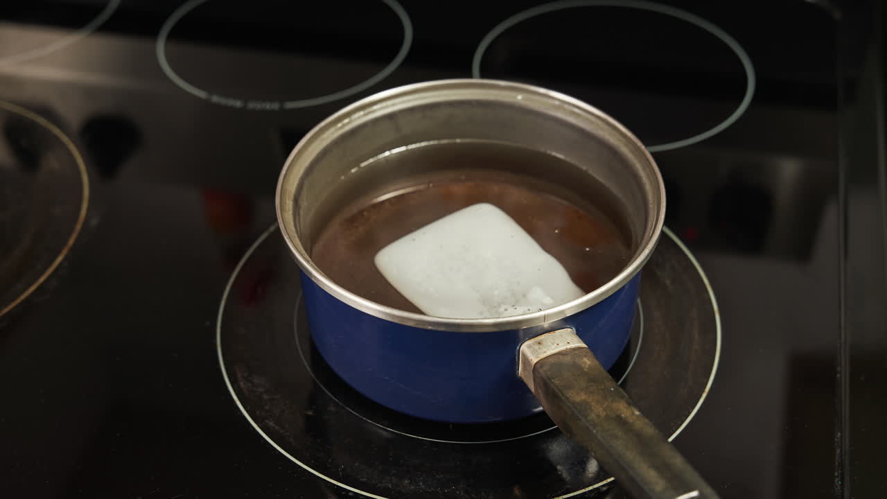Time lapse of a block of wax melting on a pan on the stove