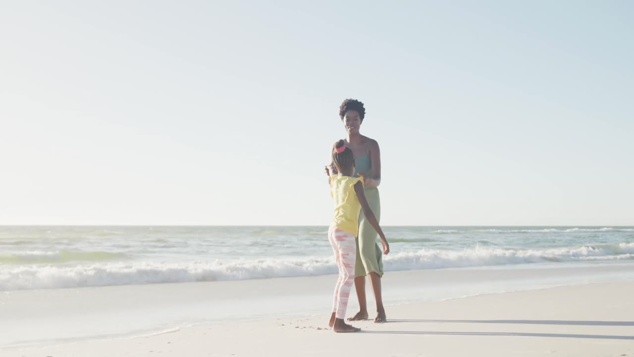 행복 한 아프리카계 미국인 어머니 와 딸 이 해변 에서 슬로우 모션 으로 춤 을 추고 있다