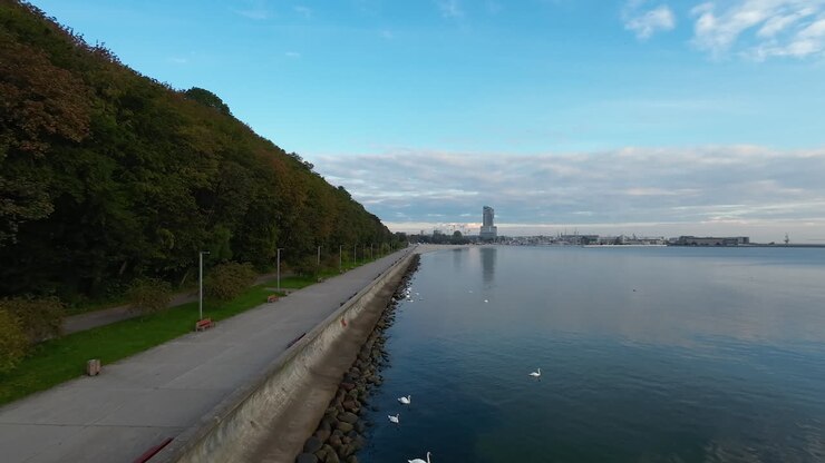 Volo di drone frontale lungo la costa del Mar Baltico con sentiero e foresta; sullo sfondo la bellissima città e il porto di Gdynia.
