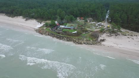 aerial establishing view of baltic sea coast on a overcast winter day, distant house at the beach with white sand, coastal erosion, climate changes, wide drone shot moving forward, camera tilt down