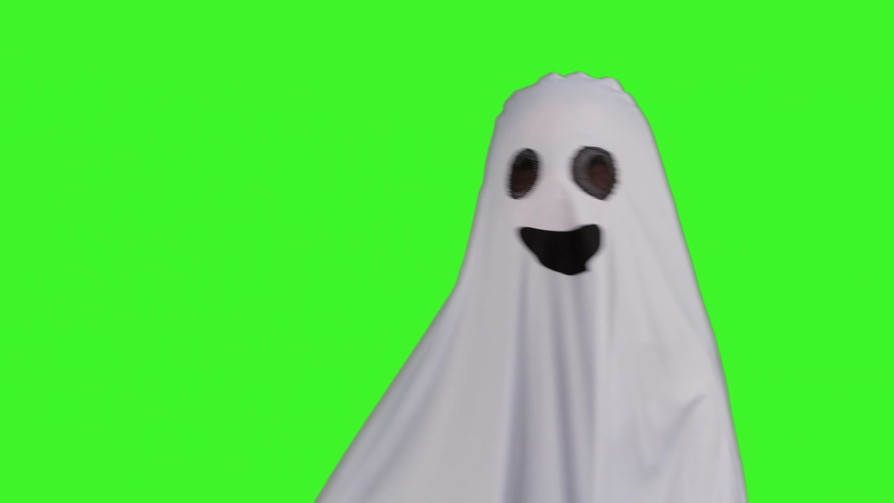 Child Dressed Up In Ghost Costume Trick Or Treating At Halloween Moving Across Frame Against Studio Green Screen