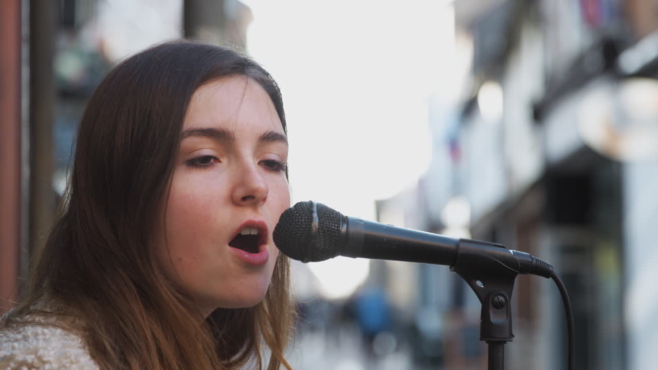 músico femenino tocando la guitarra acústica y cantando al aire libre en la calle