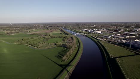 Eine-Windturbine-Für-Saubere-Energie-Wirft-Bewegte-Schatten-Auf-Ein-Feld-Auf-Dem-Land-Entlang-Eines-Binnenschifffahrtskanals-In-Den-Niederlanden,-Während-Sich-Ein-Frachtschiff-Nähert