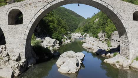 retreating drone shot revealing the arches of the devils bridgeand the arda river located in ardino, at the foot of rhodope mountains in bulgaria