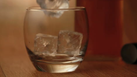 tongs placing ice into tumbler and whiskey being poured