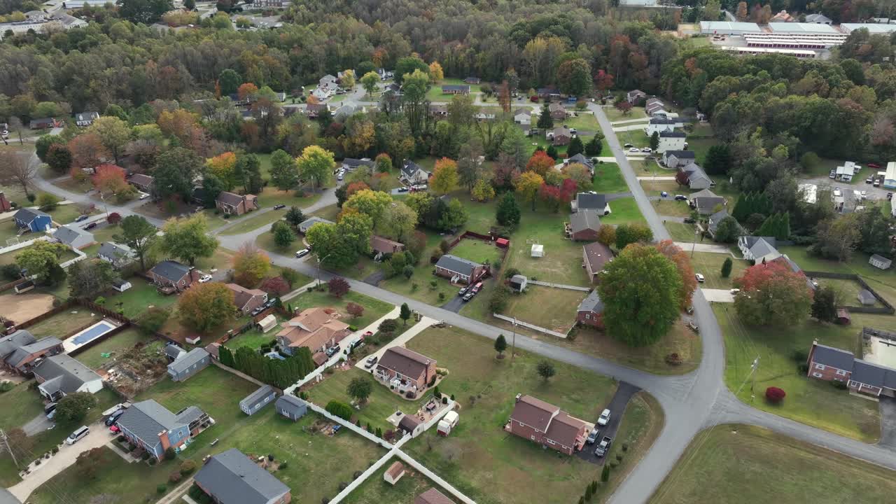Aerial orbit shot of typical american suburb neighborhood with green grass in yards and colored leaves of trees in fall. Wide shot. Street with single family houses in Virginia, USA