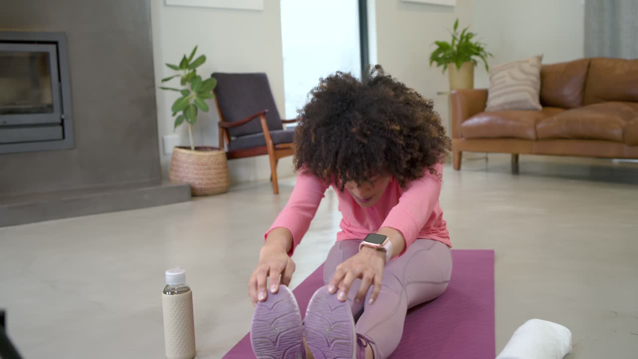 Ringlamp gaat aan, Afro-Amerikaanse vrouwelijke fitnesstrainer geeft stretchles op paarse mat thuis