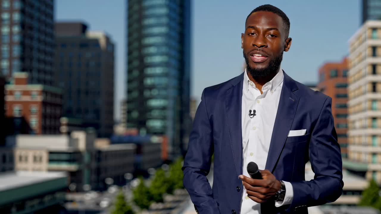 A professional video features a man in a suit speaking into a microphone, with a cityscape backdrop