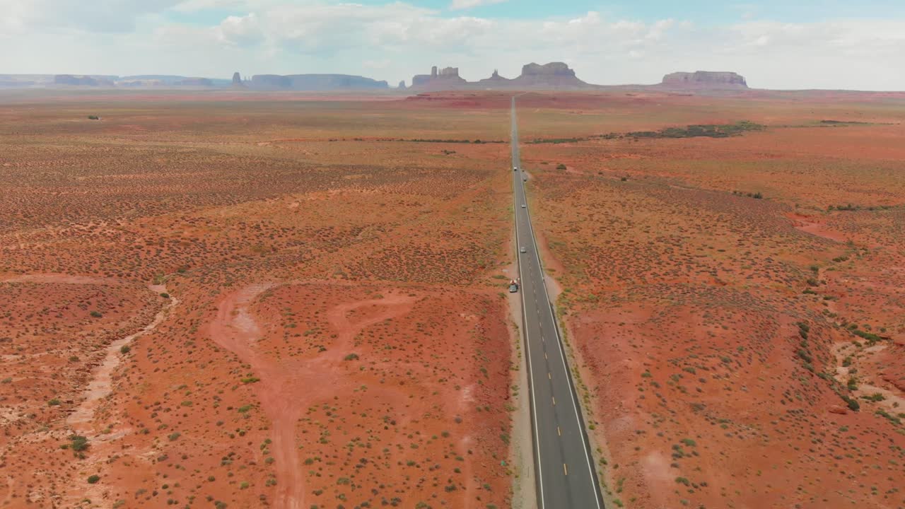 Drone follows silver car driving along famous sunny American desert highway road in Monuments Valley in Arizona and Utah