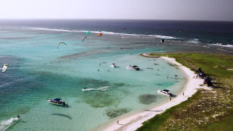 Kitesurfer-Genießen-Das-Türkisfarbene-Wasser-In-Der-Nähe-Einer-Kleinen-Insel-Mit-Booten-Und-Klarem-Himmel