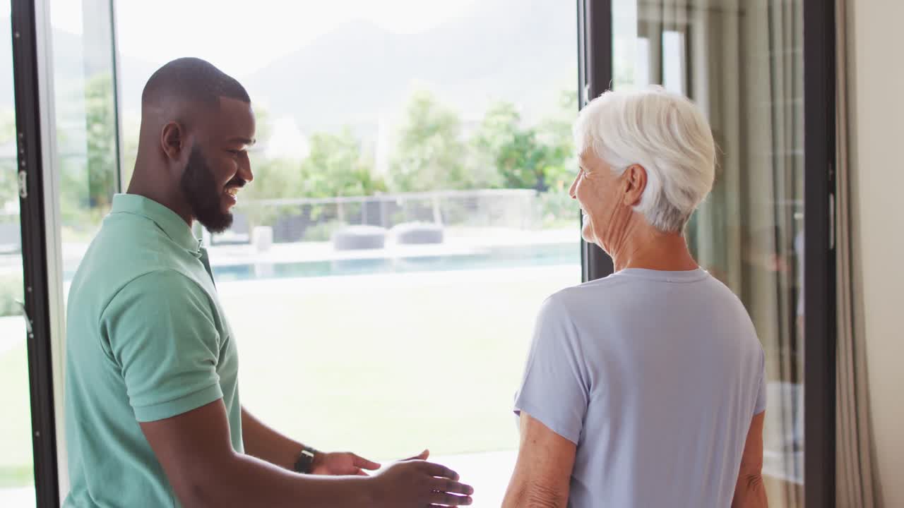 Video of happy african american male physiotherapist exercising with caucasian senior woman