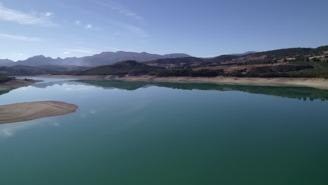 Lake with calm waters and the sky reflected in it. Mirror effect. Aerial view of a beautiful lake surrounded by mountains. Sky and clouds reflected in the lake waters. Granada. Spain
