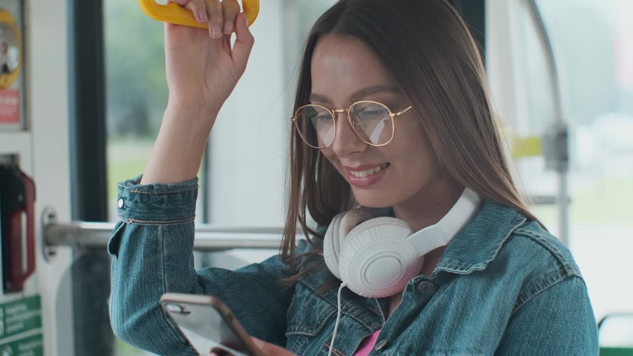 Young woman passenger standing with headphones and smartphone while moving in the modern tram, enjoying trip at the public transport.