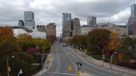 wide city street with traffic lights, cars, colorful trees and buidlings