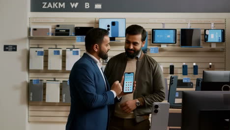 two men looking at a smartphone in an electronics store