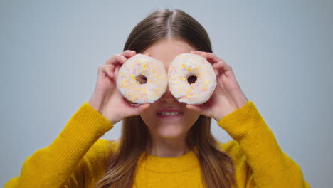 portrait of smiling woman having fun with donuts at camera on grey background.