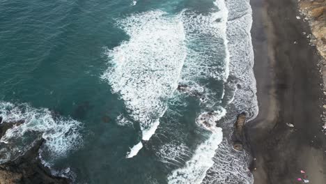 Aerial-view-of-a-black-sand-beach-with-ocean-waves-breaking-on-the-shore