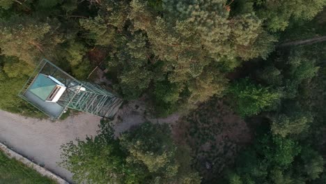 flyover old watchtower and dirt road surrounded by dense forest, top down aerial view