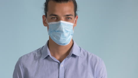 a good-looking man putting on a surgical mask isolated on light blue background - covid-19 outbreak - closeup shot