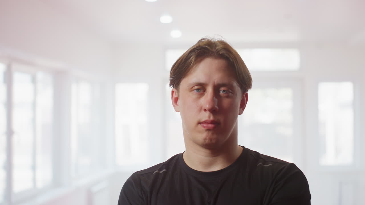 Fighter in black sportswear stands inside gym with arms crossed, projecting confidence, determination, discipline, and mental toughness, under bright natural light, readiness, and strength