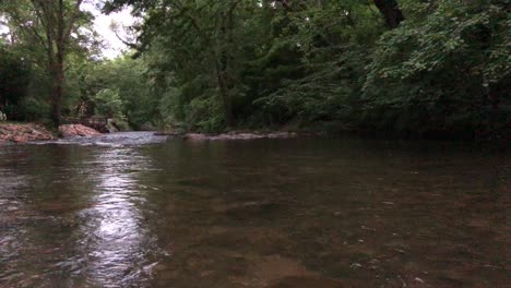 Die-Nacht-Fällt-Auf-Einen-Bedrohlich-Fließenden-Fluss,-Der-Von-Bäumen-Und-Felsen-Gesäumt-Ist