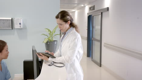 diverse female doctors using tablet and computer at hospital reception desk, copy space, slow motion