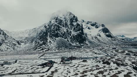 houses in winter landscape with rocky mountains in the background near flakstad in norway. aerial drone shot