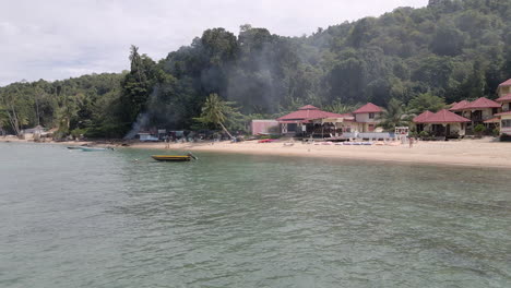 aerial drone view flying fast over the water and moored boats in front of a remote island resort and jungle. filmed at alunan resort in perhentian kecil, malaysia.