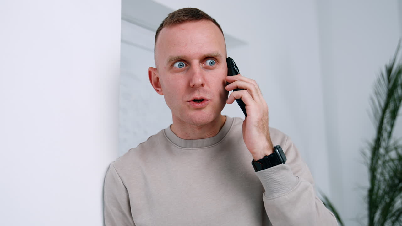 Caucasian man answering the phone call. Surprised man speaking on the smartphone and looks at his gadget with astonishment.