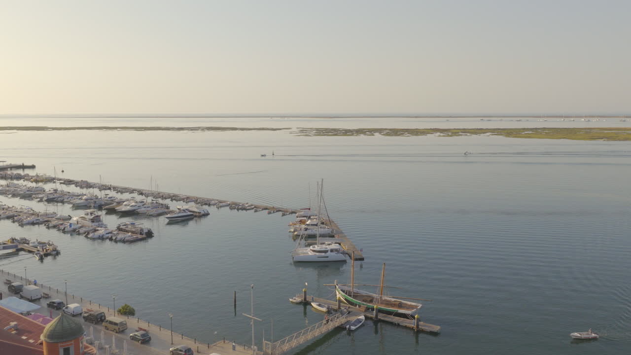 Oblique drone flight over Olhão rooftops toward marina and boats on Ria Formosa lagoon