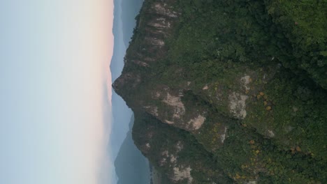 Drone-portrait-view-in-Guatemala-flying-in-front-of-a-green-mountain-surrounded-by-volcanos-on-a-cloudy-day-in-Atitlan