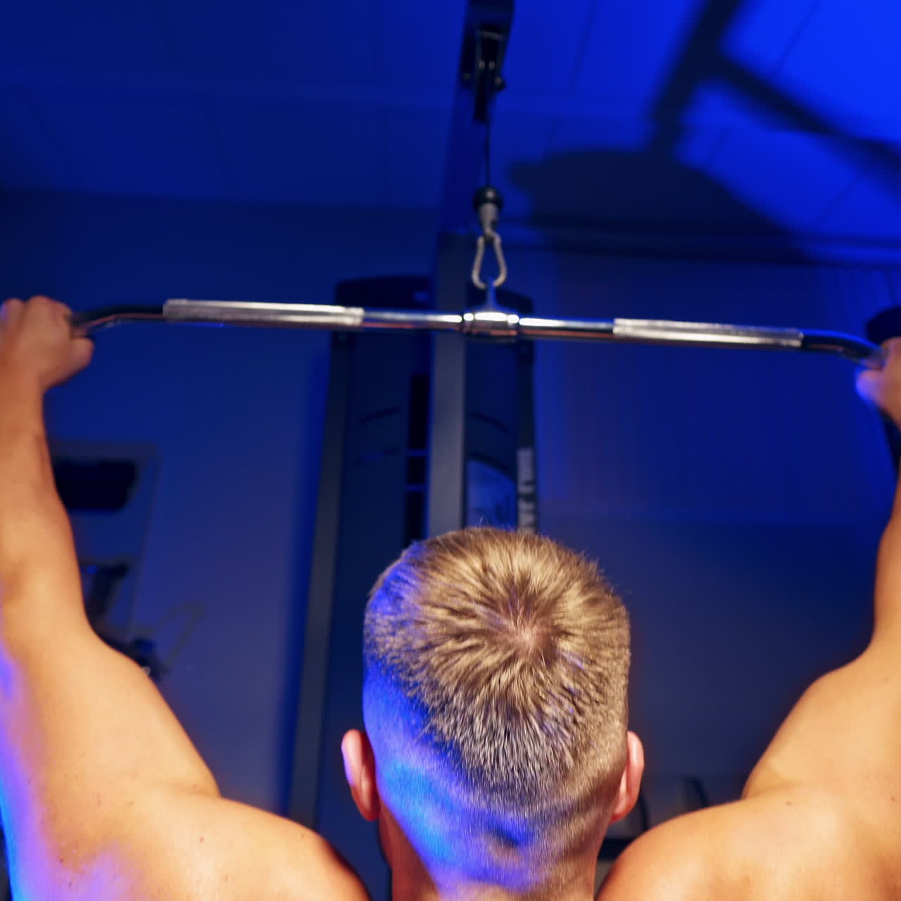 Muscular man tightening on the bar. Backside view of a strong man's body exercising in the gym on blue background. Close-up.