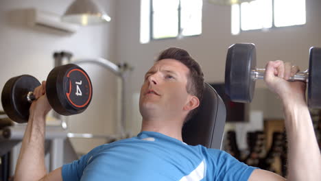 Man-works-out-with-dumbbells-on-a-bench-at-a-gym,-side-view