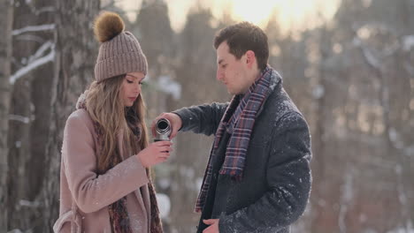 couple in love in the winter forest to drink tea from a thermos. stylish man and woman in a coat in the park in winter for a walk.