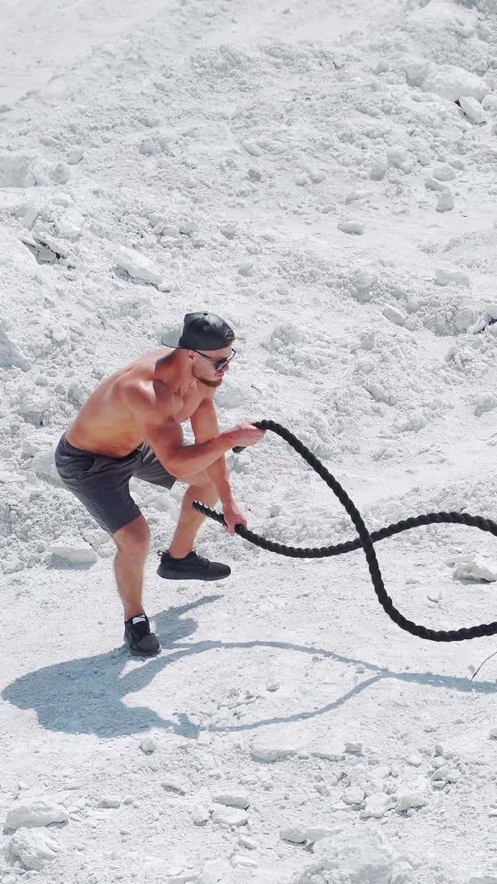 Athletic strong man doing exercises with ropes outdoors on the sand. Shirtless bodybuilder training. Vertical video