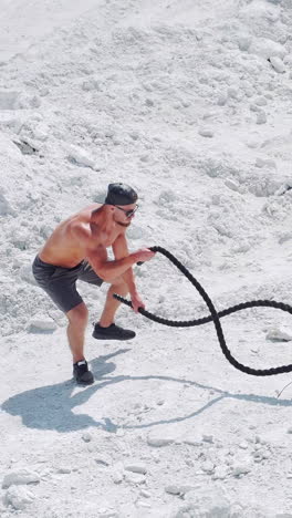 athletic strong man doing exercises with ropes outdoors on the sand. shirtless bodybuilder training. vertical video