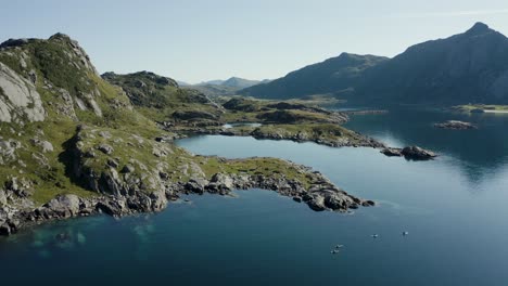 aerial drone shot of scandinavian landscape with group of paddle boarders, dramatic mountains, ocean and verdant greenery