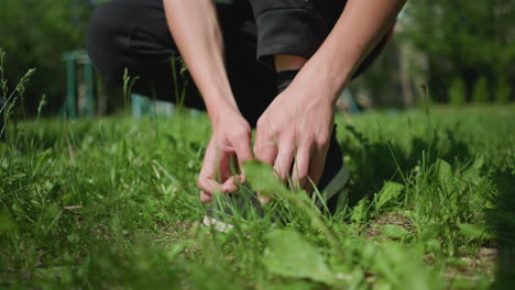 close-up of someone adjusting their shoes while kneeling on a grassy field, focusing on the hands and footwear