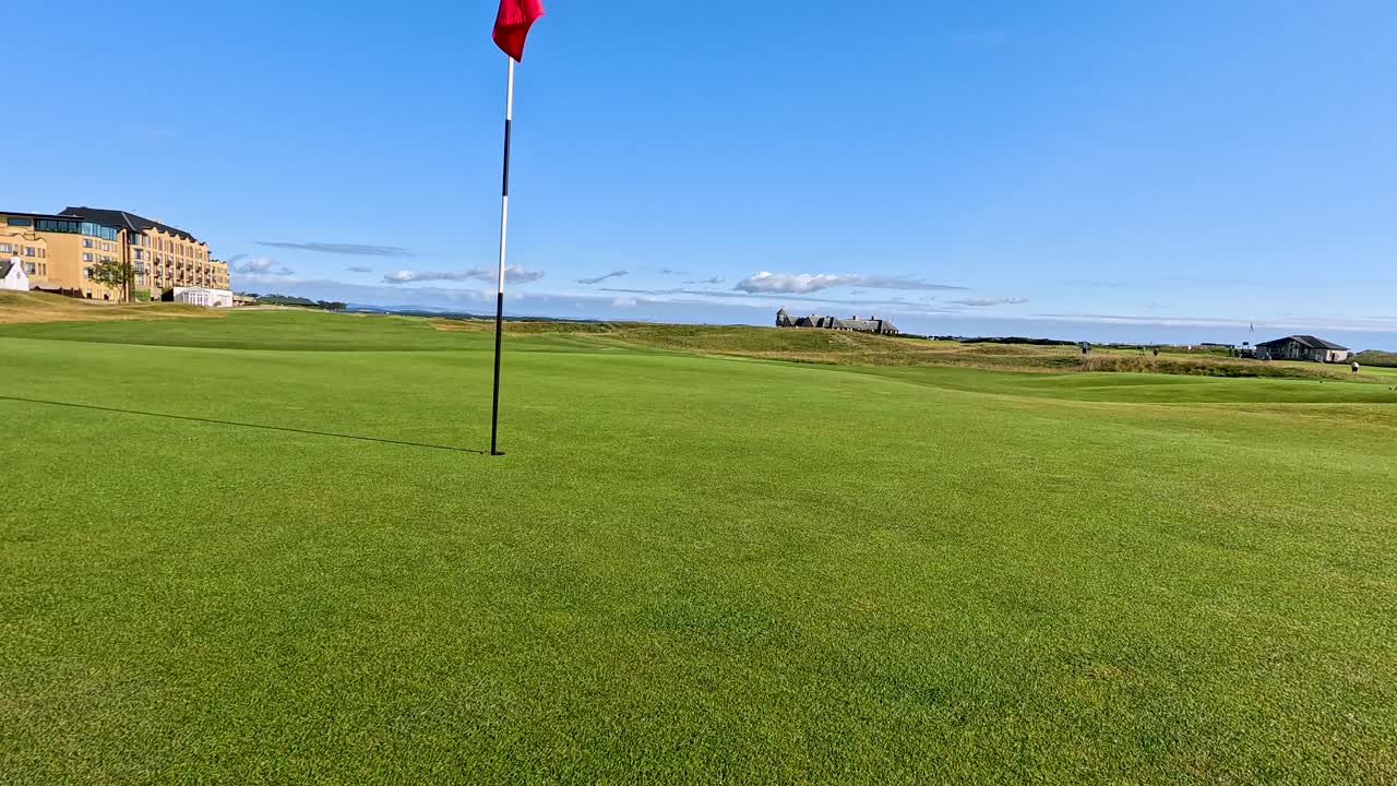 Camera dolly toward golf flag on lush green, bright daylight, clear sky, resort backdrop