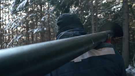 worker carrying long pipe through snowy forest