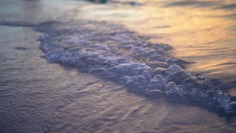 Der-Sonnenuntergang-Spiegelt-Sich-In-Kleinen-Meereswellen-Wider,-Die-Sanft-Auf-Einen-Sandstrand-Rollen
