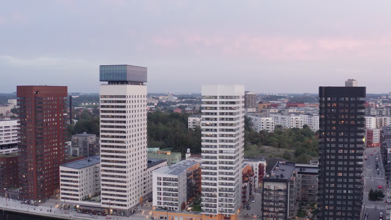 Drone footage of four high-rise residential buildings with modern design and architecture in &Aring;rstadal, Stockholm during sunset with pink sky and sun as background