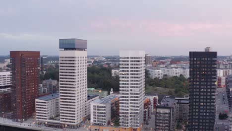 Drone-footage-of-four-high-rise-residential-buildings-with-modern-design-and-architecture-in-Årstadal,-Stockholm-during-sunset-with-pink-sky-and-sun-as-background
