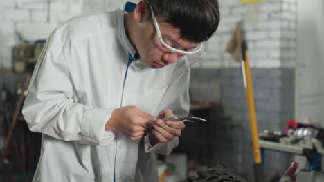 young technician in automotive workshop carefully measuring engine thickness using vernier caliper. focused expression as he shows measurement reading to someone nearby