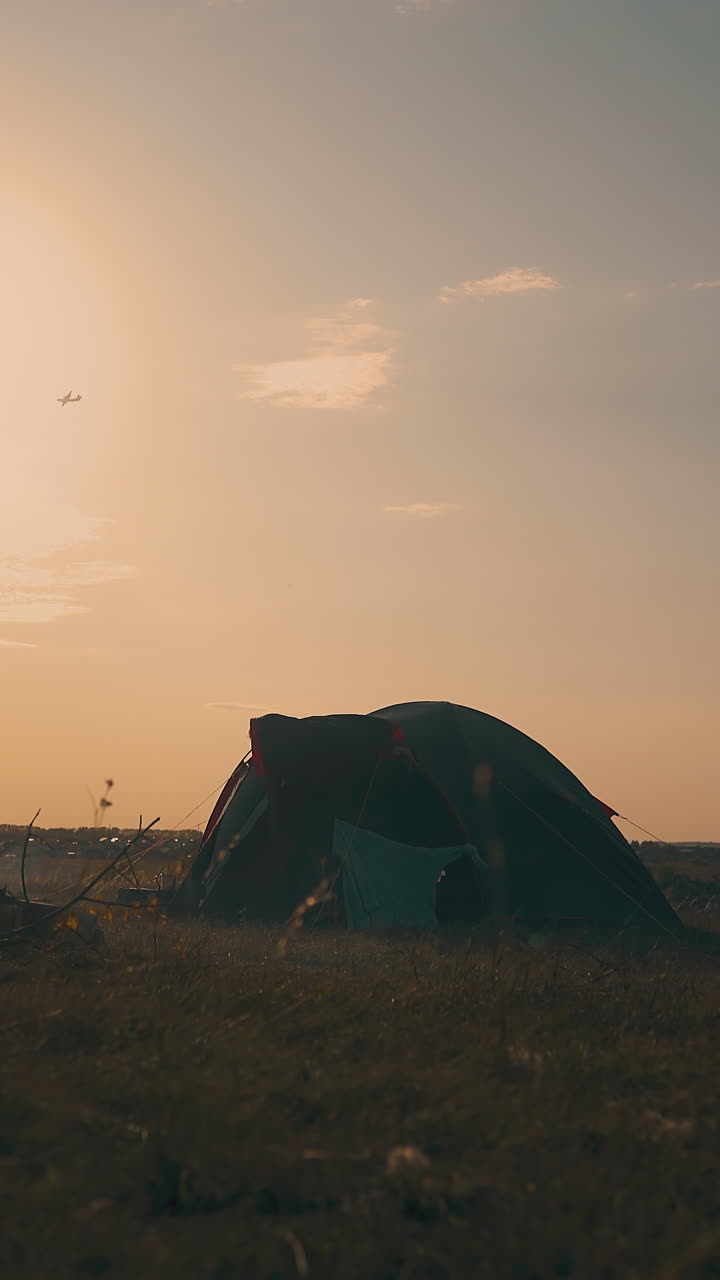 silhouette of young man going out of tent in camp on river bank in autumn morning at sunrise against boundless sky