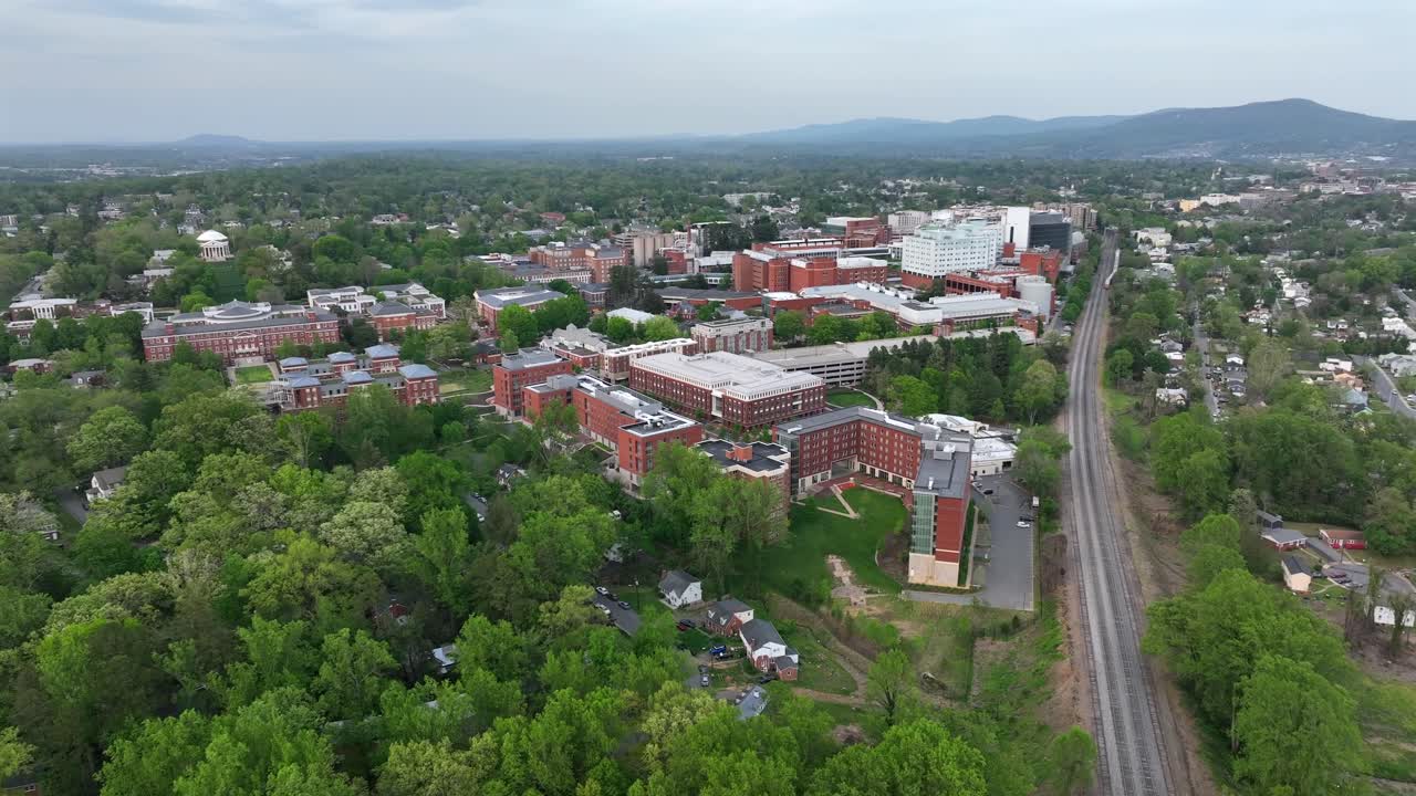 Green trees between red brick University of Virginia during Cloudy day. Railroad tracks in Charlottesville, USA. Aerial wide shot. Historic buildings on campus area.
