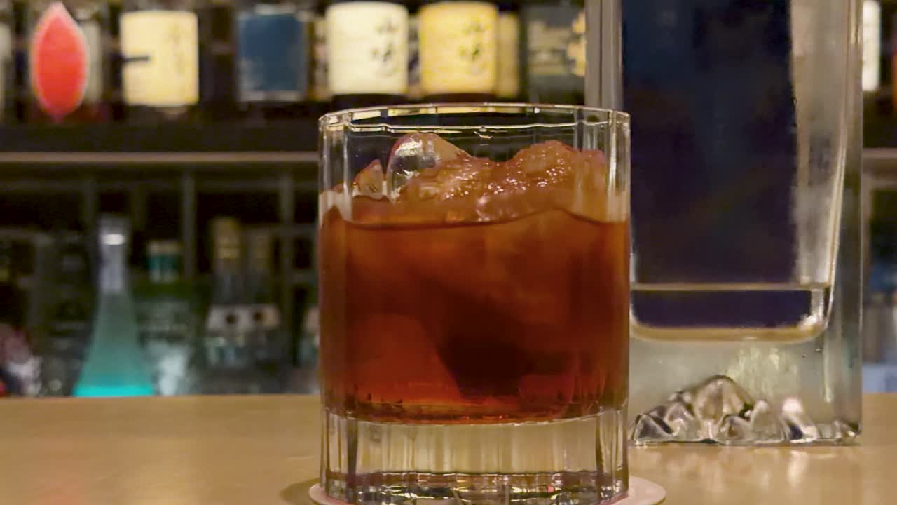 Un primo piano di un cocktail Negroni con cubetti di ghiaccio su un bancone da bar in legno.